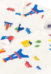 Ensemble pour bébé en coton blanc avec des imprimés colorés de voitures, de maisons et d'un carrousel, avec des accents rouges, bleus, jaunes et verts.