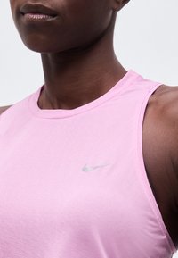 Gros plan d'une personne portant un haut rose sans manches Nike avec un petit logo réfléchissant Nike sur la poitrine.