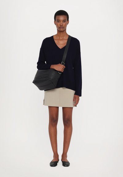 Navy v-neck sweater and beige skirt worn with black shoulder bag and flats. Smooth textures, relaxed fit, and shoulder strap detail visible.