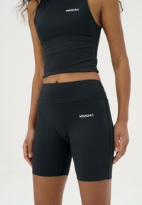 Zwarte sportieve crop top en hoge taille shorts, gemaakt van rekbaar materiaal, met een wit merklogo en een gladde textuur.