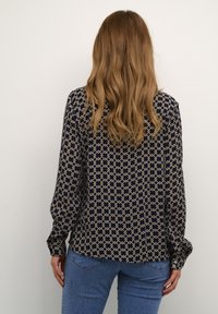 Blusa navy con un motivo geometrico beige, maniche lunghe, polsini con bottone e una vestibilità rilassata, abbinata a jeans blu.