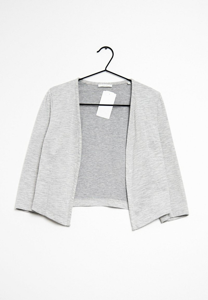 Cardigan gris clair ouvert sur le devant avec manches longues suspendu sur un cintre noir avec une étiquette de prix blanche au niveau de l'encolure.
