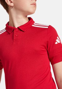 Rode polo shirt van gestructureerd materiaal, met een kraag, twee knopen en witte strepen op de mouwen. Inclusief een logodetail.
