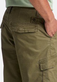 Pantaloni cargo verde oliva realizzati in tessuto resistente, dotati di tasche laterali, un design cucito e una toppa con il logo Timberland sul retro.