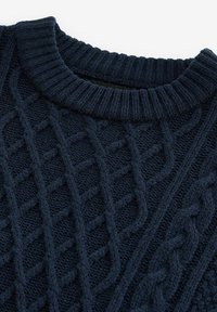 Granatowy sweter z dzianiny o fakturowanym splocie w warkocz i prążkowanym okrągłym dekolcie. Widoczne szwy tworzą gęsty, przytulny wygląd.