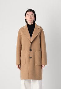 Beige gyapjúpulóver, kilapított gallérral, három gombbal és két elülső zsebbel. Puha tapintású, lazán illeszkedő szabású, hosszú ujjú.