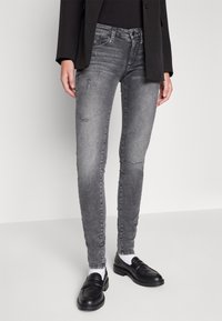 Jeans ajustados de mezclilla gris con detalles desgastados, cintura media y silhouette entallada, combinados con mocasines negros y calcetines blancos.
