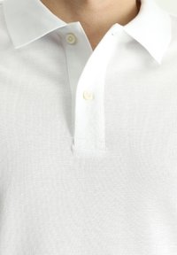 Polo bianco realizzato in tessuto testurizzato, con colletto standard, due bottoni al collo e un design semplice e pulito.