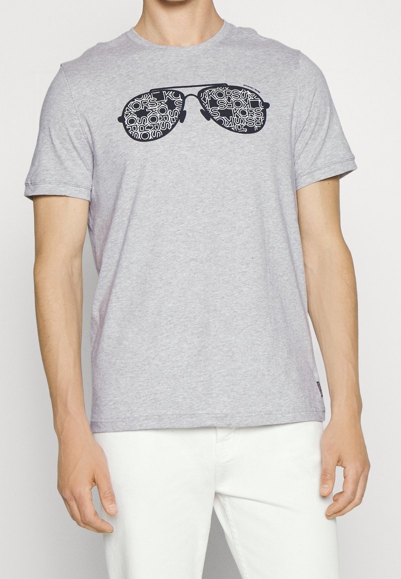 Camiseta gris de manga corta con un gráfico negro de gafas de sol con un patrón de texto repetido. La tela es una mezcla suave de algodón.