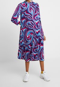 Wielokolorowa sukienka z wirującym wzorem w odcieniach niebieskiego, różowego i fioletowego, wykonana z gładkiego materiału z okrągłym dekoltem i długimi rękawami.
