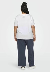 Valkoinen lyhythihainen t-paita, jossa on pyöreä kaula-aukko. Takana pieni painettu teksti. Yhdistetty tilaviin laivastonsinisiin housuihin ja lenkkareihin.