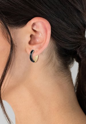 Boucle d'oreille noire avec une accent dorée, alliant finition brillante et texture lisse. Conçue pour épouser confortablement le lobe de l'oreille.