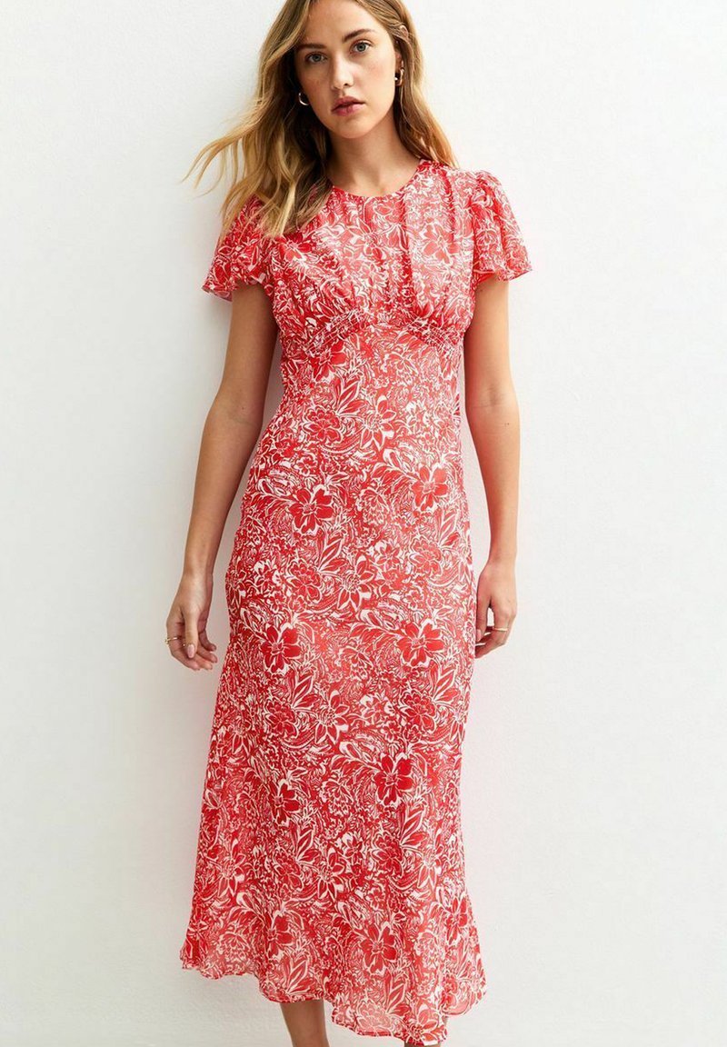 Robe fleurie rouge avec des manches courtes et volantes, présentant un bustier ajusté et un ourlet évasé. Le motif comprend des fleurs blanches et du feuillage.