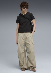 Zwarte katoenen T-shirt met logo, beige cargobroek met zijzakken, gecombineerd met een donkere zonnebril en een zwarte tasriem met ruches.