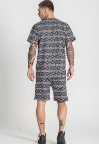 Čierna a biela vzorovaná súprava trička a šortiek so geometrickými motívmi. Materiál sa zdá byť pohodlný. Nosí sa s čiernymi teniskami.