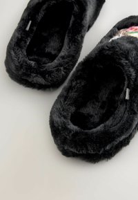 Black faux fur slippers with a soft, plush texture, rounded design, and open back. Features embroidered decorative accents in color.