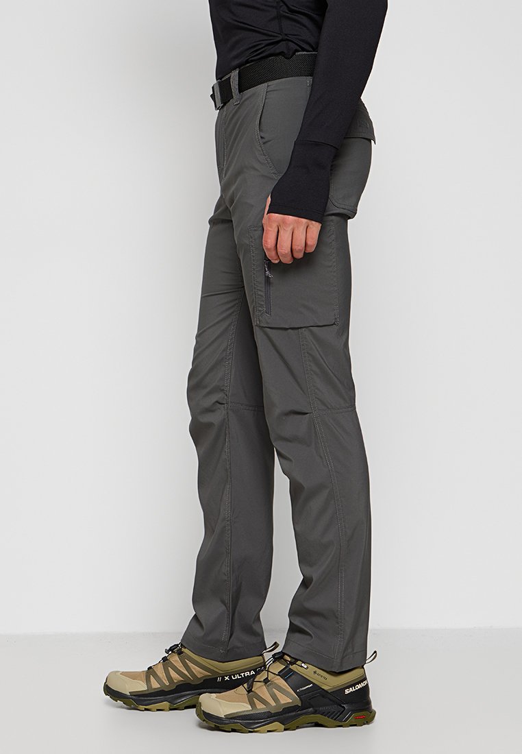 Graue Outdoor-Hosen mit geradem Schnitt, ausgestattet mit mehreren Taschen und verstärkten Nähten. Kombiniert mit beigen Wanderschuhen.