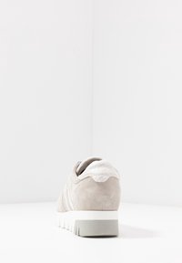 Beige nahkaiset wedgesneakerit, joissa on valkoiset strukturoidut kantatiedot ja paksu harmaa-valkoinen pohja, valkoisella pinnalla.