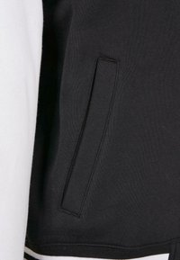 Black and white sweatshirt featuring a side pocket, ribbed hem, and smooth texture with contrasting colored sleeves.