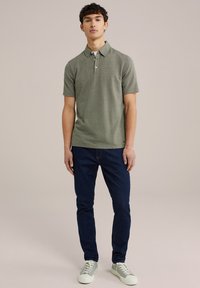 Polo verde cu mânecă scurtă, având un model texturat și guler, asortat cu blugi negri și adidași verzi deschis. Croială simplă și casual.