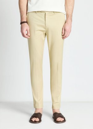 Uomo che indossa pantaloni beige slim fit, sandali intrecciati marrone scuro, camicia bianca e un braccialetto marrone sul polso sinistro.