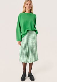 Zelený oversize pletený sveter skombinovaný so zeleno-bielou prúžkovanou midi sukňou. Čierne mokasíny a priesvitné čierne pančuchy dotvárajú outfit.