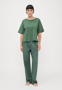 Groene katoenen t-shirt met korte mouwen, gecombineerd met bijpassende losse broek in een gladde stof. Heeft simpele, schone lijnen en geen zichtbare patronen.
