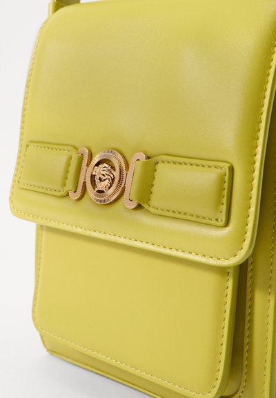 Borsa a tracolla in pelle verde lime con una texture liscia, caratterizzata da un'emblema dorato a forma di leone e una chiusura con cinghie decorative.