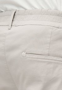 Pantalon beige clair avec une ceinture élastique, doté d'une poche arrière avec bordure contrastante et en tissu de coton lisse.