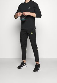 Musta urheiluasu, johon kuuluu pitkähiha-paita ja kapeat housut neonkorostuksilla; kädessä kettlebell; mustat juoksukengät.