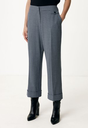 Mujer con pantalones cortos de pata de gallo en blanco y negro con dobladillos remangados y botines negros de tacón.