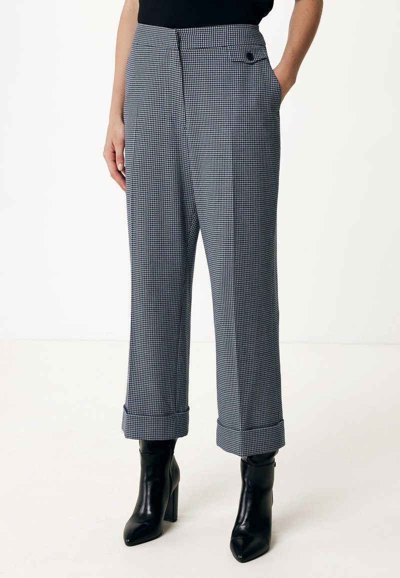 Femme portant un pantalon court imprimé pied-de-poule noir et blanc avec ourlets retroussés et bottines noires à talons.