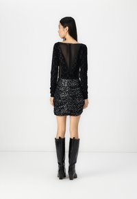 Body nero in tessuto strutturato, schiena trasparente e maniche lunghe abbinato a una mini gonna nera a paillettes arricciata. Stivali neri al ginocchio.