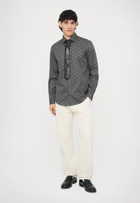 Μαύρο πουκάμισο με σχέδιο και μακριά μανίκια, με μυτερό γιακά, συνδυασμένο με κρεμ παντελόνια και μαύρη γραβάτα, ολοκληρωμένο με μαύρα παπούτσια.