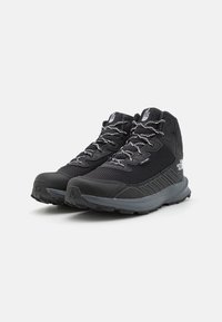 Chaussures de randonnée noires avec des matériaux en maille et en caoutchouc, design montante, surface texturée, lacets réfléchissants et un logo bien en vue sur le côté.