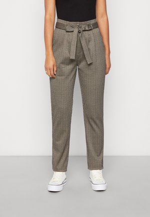 Woman wearing high-waist checkered trousers tied with a front bow, paired with white sneakers and a black sleeveless top.