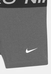 Shorts de sport gris avec une ceinture noire portant le texte "NIKE" en blanc. Petit logo Nike swoosh blanc en bas à droite. Texture lisse.