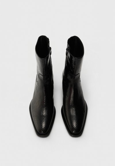 Botas de tobillo negras hechas de cuero sintético texturizado de serpiente. Diseño de punta afilada con cremallera lateral para facilitar su uso. Acabado liso y brillante.