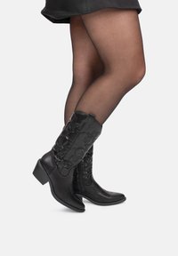 Botas de cuero negro hasta el tobillo con diseño floral bordado, punta cuadrada y tacón bajo. Cierre lateral con cremallera para facilidad al vestir. Acabado semibrillante.