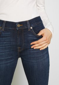 Donkerblauwe denim jeans met subtiele vervaging, contrasterende stiknaden, een klassiek vijfzakkenontwerp en een metalen knoopsluiting.