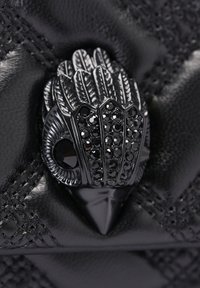 Accessorio in pelle nera con un fermaglio dettagliato dal design simile a una piuma, arricchito da strass neri e una finitura lucida.