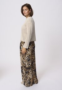 Pull en maille beige à coupe décontractée et manches longues, associé à un pantalon large en imprimé animal noir, marron et crème.