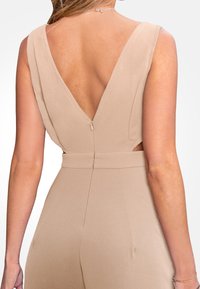 Tuta nude con profondo scollo a V sul retro, design senza maniche, ritagli laterali e chiusura con zip. Tessuto liscio con una vestibilità strutturata.