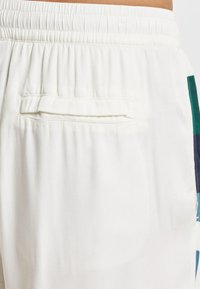 Vaaleanväriset, tekstuurilliset kangasshortsit, joissa on joustava vyötärönauha ja takatasku, jossa on litteä taskun suuaukko.