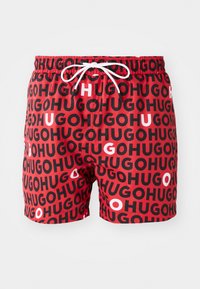Rote Badeshorts mit einem sich wiederholenden schwarz-weißen "HUGO"-Muster und einem weißen Kordelzug am elastischen Bund.