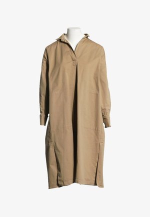 Longue robe-chemise beige à manches longues, col montant, fente devant et fentes latérales, présentée sur un buste de mannequin blanc.