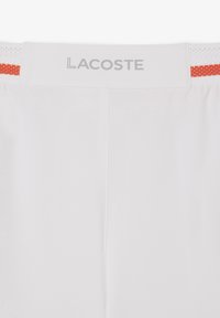 Pantaloni corti bianchi Lacoste con una cintura testurizzata che presenta un accento arancione, materiale leggero e dettagli cuciti sul retro.