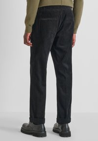 Pantaloni in velluto a coste neri con vestibilità affusolata, caratterizzati da un motivo testurizzato, due tasche posteriori e orli arrotolati, abbinati a scarpe nere con lacci.