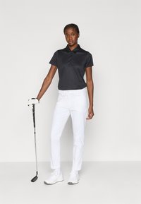 Crna polo majica s kragnom i dugmadi, uparen s bijelim hlačama. Model drži golf palicu, nosi bijele tenisice i rukavicu.