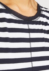 T-shirt w niebiesko-białe paski z okrągłym dekoltem, kontrastującymi czarnymi szwami oraz miękką fakturą materiału.